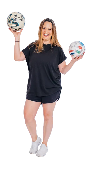 Mag. Birgit Hütter steht lächelnd in Sportoutfit und hält zwei Fussbälle in den Händen – aktiv, spielerisch und voller guter Laune.