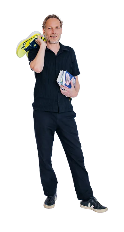 Dr. Thomas Winder trägt ein Paar Laufschuhe lässig über der Schulter und hält mehrere Bücher im Arm – sportlich, wissbegierig und stets in Bewegung.