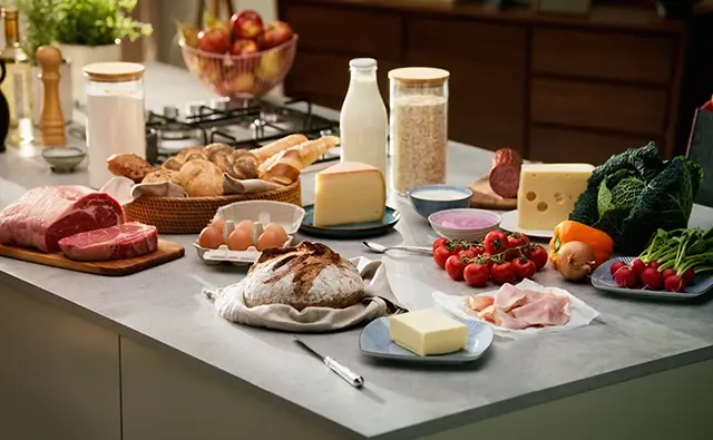 Fresh produce on a modern kitchen counter, including regional products like bread, milk, eggs, meat, vegetables, and cheese. Symbolic image for AMA marketing campaigns on quality and origin of Austrian food.