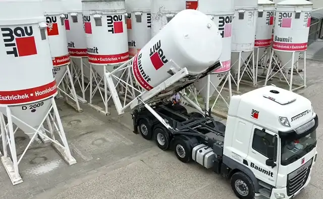 Baumit truck delivers a silo container to a company site with several building material silos.