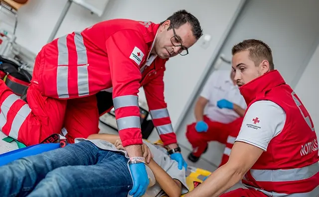 Paramedics of the Austrian Red Cross performing first aid. Image emphasizes humanitarian commitment and medical care competence.