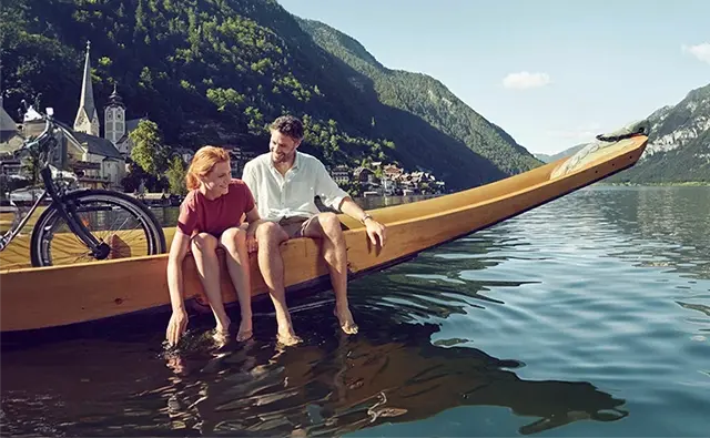 Couple relaxing on a traditional wooden boat in Lake Hallstatt with a view of the Alps. Depiction of idyllic Austrian summer landscape for tourism marketing.