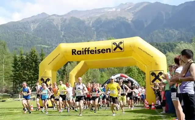 Runners start at a city marathon under a yellow Raiffeisen Bank archway.