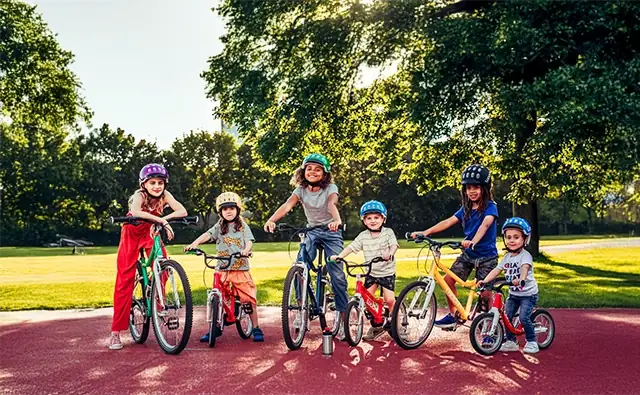 Six children of different ages and skin colors on colorful Woom bikes in a sunny park. Symbolic image for strong brand presence and global growth in various markets.