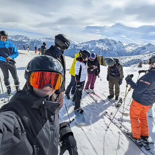 Group of colleagues at Snow Academy 2025, on a ski slope, ready to descend - with impressive mountain scenery in the background and sunny weather.