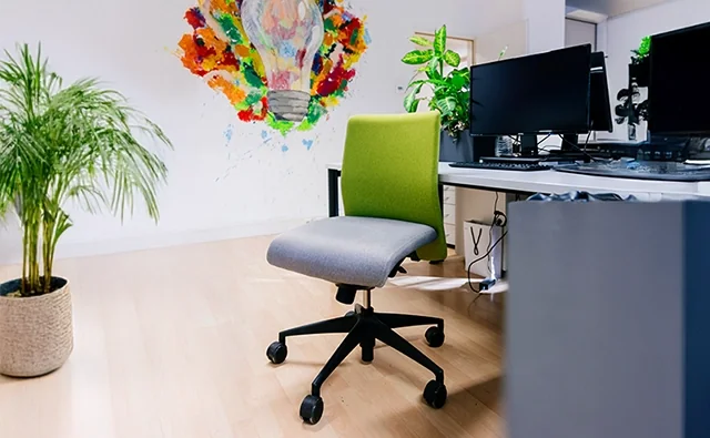 Empty office chair with green upholstery in front of a workstation with several computer screens in the marketmind office.