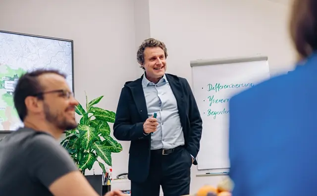 Gereon Friederes stands in front of a flipchart and speaks to a group of people in a meeting room. The terms differentiation, credibility, and enthusiasm are written on the flipchart.