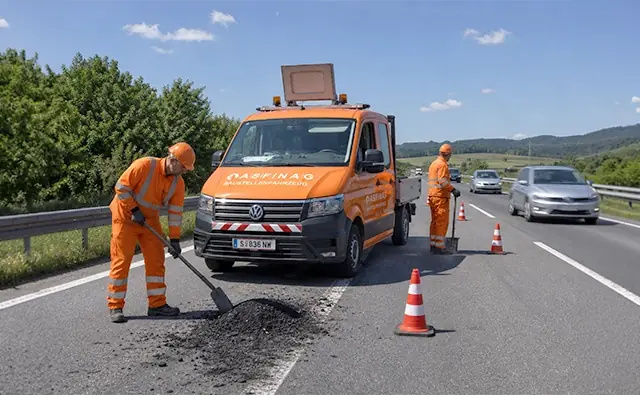 ASFINAG roadwork vehicle and employees in high-visibility clothing secure a work area on the motorway with traffic cones. Image represents road safety, road maintenance, and reliable infrastructure support.