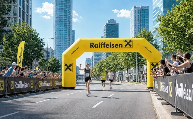 Runners start at a city marathon under a yellow Raiffeisen Bank archway.