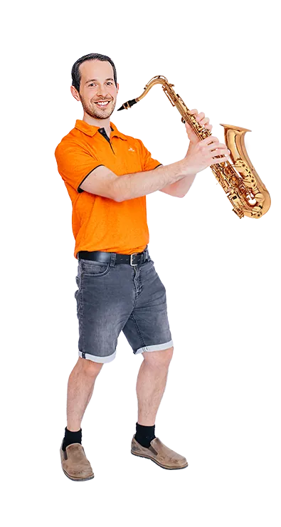 Andreas Kritsch stands with a saxophone in his hands and smiles at the camera - musical, humorous, and full of playfulness.