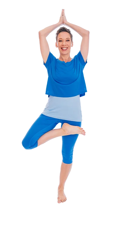 Dagmar Jiresch stands barefoot in tree position and wears a blue yoga outfit - full of balance, energy, and inner peace.