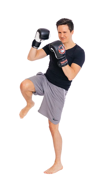 Daniel Mader stands in fighting stance with boxing gloves and raises the knee - focused, energetic, and athletic.