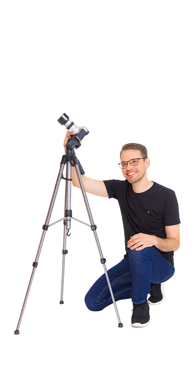 Daniel Winzer kneels smiling next to a tripod with camera - with passion for photography and the perfect moment.