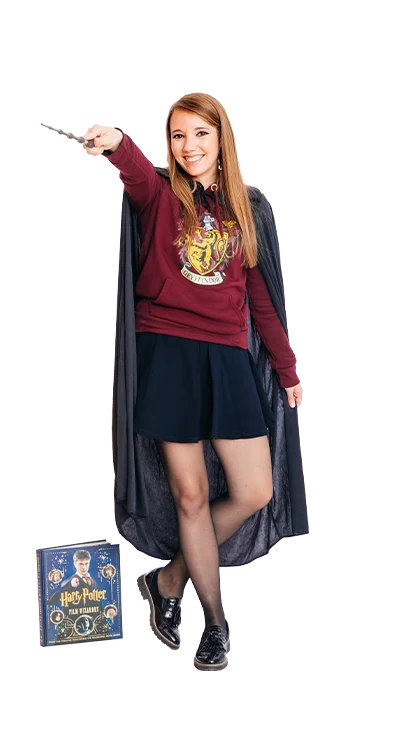 Jana Eisenbock stands in a Harry Potter costume with cloak and wand, a board game on the floor - imaginative, immersed in the world of magic.