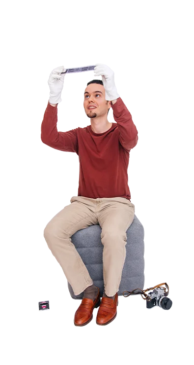 Jan-Bartl Koncel sits on a stool and wears white gloves while examining a photo negative against the light - with love for analog photography.