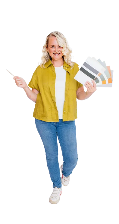 Kerstin Hofer stands with color fan and brush in hand and smiles enthusiastically at the camera - creative, vivacious, and full of design passion.