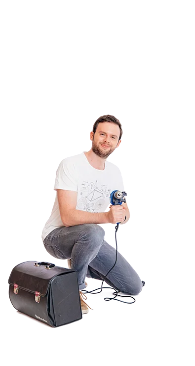 Lucas Pum crouches with drill in hand next to a bag, wears jeans and T-shirt - technology-enthusiastic, creative, and focused.