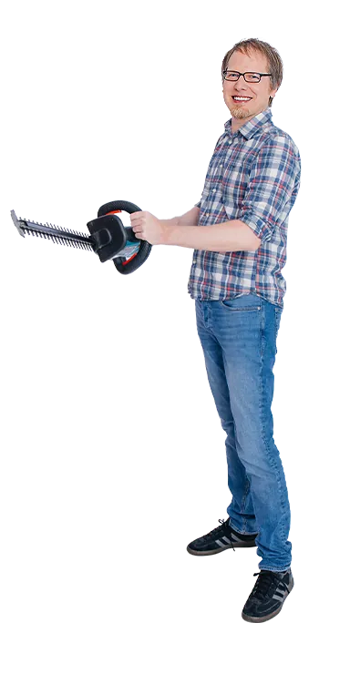 Martin Fuchs stands with hedge trimmers in his hands and smiles at the camera - committed, down-to-earth, and with a sense for practical tasks.
