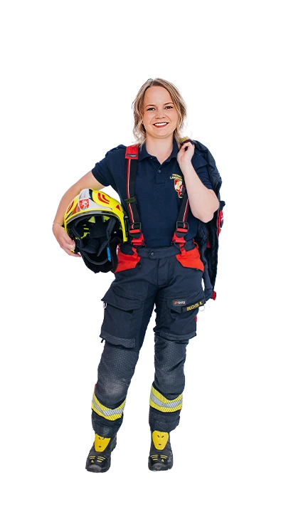 Nadine Buchta wears dark blue firefighter trousers with red suspenders and yellow reflective stripes, carrying a firefighter helmet under one arm and the turnout jacket over her shoulder - passionate about the volunteer fire brigade.