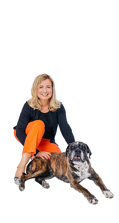 Dr. Verena Priemer kneels smiling next to a brown dog, places her hand on its back, and radiates calm and connection - animal-loving, warm-hearted, and full of positive energy.